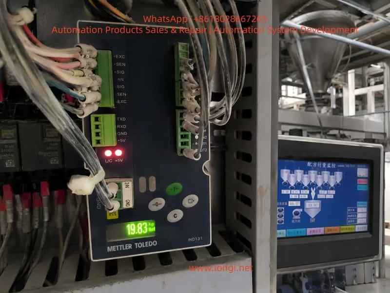 Close-up of a METTLER TOLEDO IND131 weighing module inside an industrial control cabinet displaying 19.83 kg during a 20 kg test weight check, with the batching machine HMI and weigh hopper shown in the background.