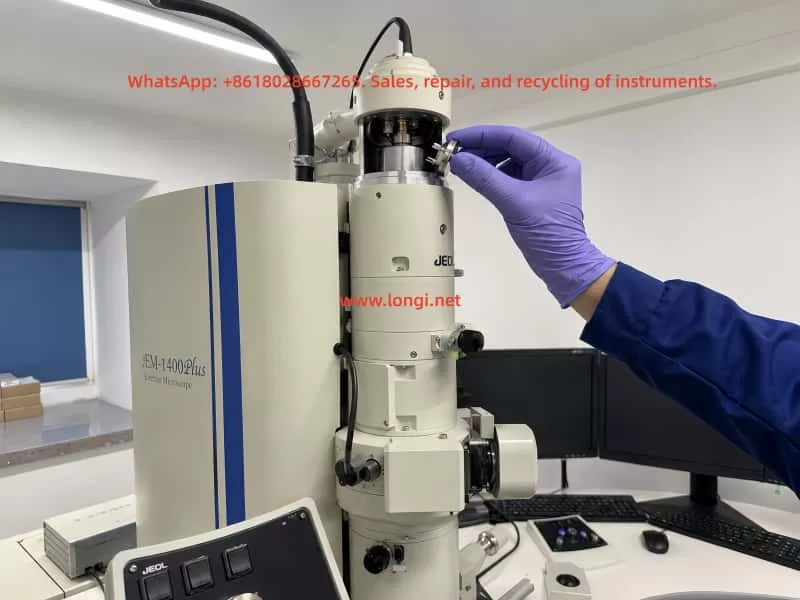 Engineer wearing protective gloves installing a tungsten filament assembly into the electron gun of a JEOL JEM-1400 transmission electron microscope during maintenance and alignment procedure.