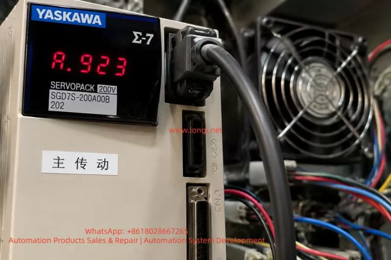 Close-up view of a Yaskawa Σ-7 SERVOPACK inside an industrial electronics enclosure, showing a red A.923 error code on the display, surrounded by connectors, colorful wires, and a cooling fan, highlighting the internal components of the servo drive.