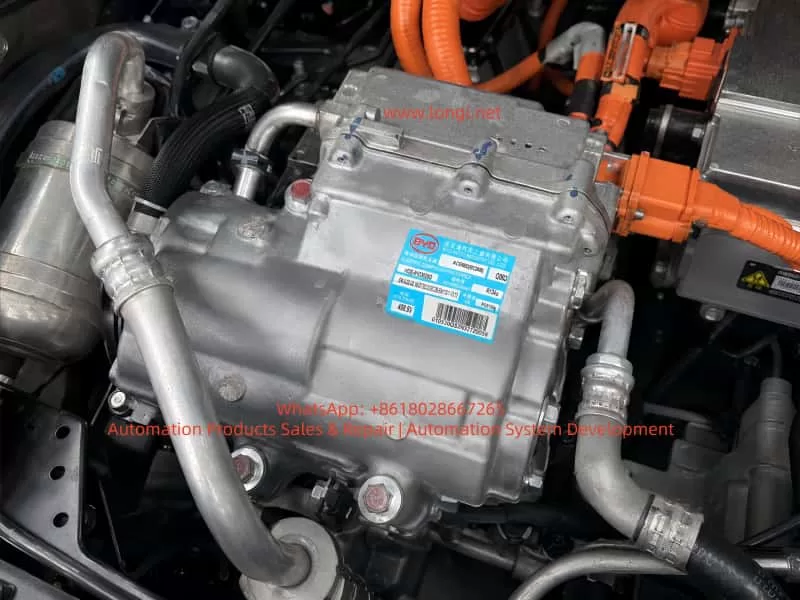 Close-up of a BYD high-voltage electric A/C compressor assembly installed in an electric vehicle, showing the aluminum compressor housing, R134a refrigerant pipes, orange high-voltage cables, and identification label.